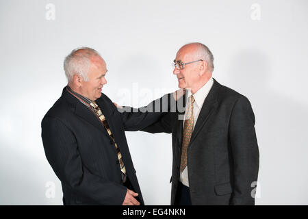 two senior businessmen friends smiling and shaking hands and shoulders Stock Photo