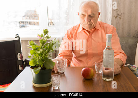 Close up Lonely Sitting Elderly Drinking Wine at the Table with Apple and Green Plant on Top. Stock Photo