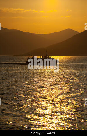 Looking across the Firth of Clyde, towards the Argyle hills at sunset with boat silloeted against light. Stock Photo