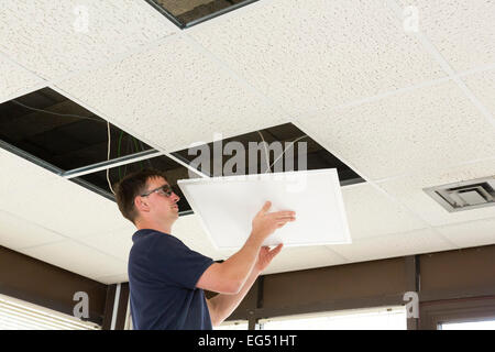 electrician installing LED flat panel lighting in a suspended ceiling Stock Photo
