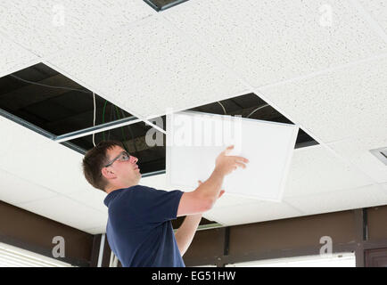electrician installing LED flat panel lighting in a suspended ceiling Stock Photo
