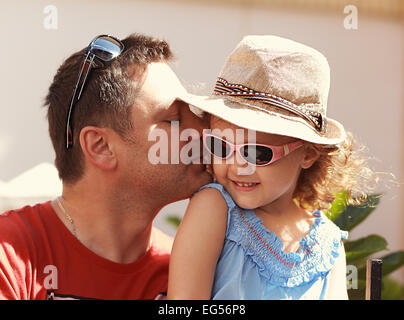 Loving father kissing his happy child girl in sun glasses on nature summer background Stock Photo