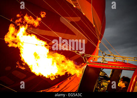 Man controlling gas burner flames inflating red hot air balloon, South Oxfordshire, England Stock Photo