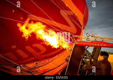 Man controlling gas burner flames inflating red hot air balloon, South Oxfordshire, England Stock Photo