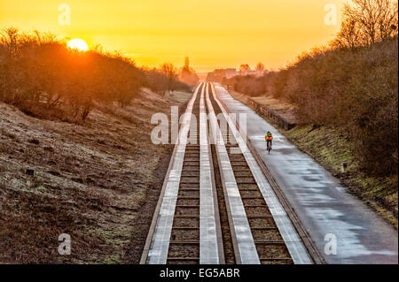 Over, Cambridgeshire 17th February 2015.  A lone cyclist heads towards Cambridge as the sun rises on the Cambridgeshire Guided Busway on a cloudless frosty morning. Sunshine is forecast for much of the UK today.  The guided busway runs between Cambridge and St Ives and is the longest in the world. It provides a track for buses and a path for pedestrians and cyclists across the flat landscape north of Cambridge. Credit Julian Eales/Alamy Live News Stock Photo