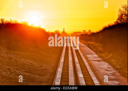 Over, Cambridgeshire 17th February 2015.  A bus heads towards Cambridge as the sun rises on the Cambridgeshire Guided Busway on a cloudless frosty morning. Sunshine is forecast for much of the UK today.  The guided busway runs between Cambridge and St Ives and is the longest in the world. It provides a track for buses and a path for pedestrians and cyclists across the flat landscape north of Cambridge. Credit Julian Eales/Alamy Live News Stock Photo