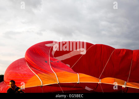 Man controlling billowing red hot air balloon, South Oxfordshire, England Stock Photo