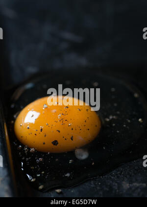 Cracked chicken egg with black pepper on dark background, selective focus Stock Photo