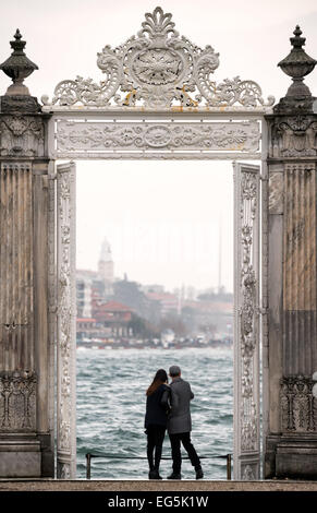 ISTANBUL, Turkey (Turkiye) — A couple stands under one of the ornately decorated gates at Dolmabahçe Palace looking out over the Bosphorus Strait toward the Asian coast. Dolmabahçe Palace, on the banks of the Bosphorus Strait, was the administrative center of the Ottoman Empire from 1856 to 1887 and 1909 to 1922. Built and decorated in the Ottoman Baroque style, it stretches along a section of the European coast of the Bosphorus Strait in central Istanbul. Stock Photo