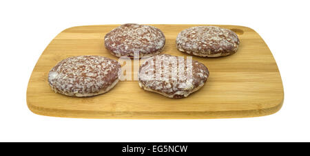 Side view of several glazed gingerbread cookies on a wood cutting board atop a white background. Stock Photo