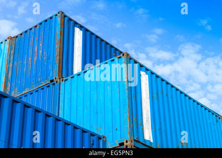 Blue metal Industrial cargo containers are stacked in the storage area under blue cloudy sky Stock Photo