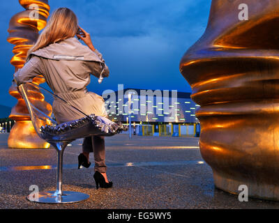 Girl seen from behind telephoning outdoors in square with modern architecture Stock Photo
