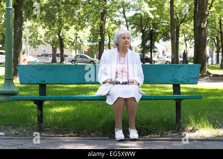 83 years old elderly woman sitting on a bench in a park Stock Photo