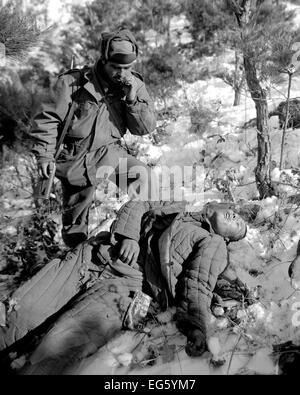 KOREAN CONFLICT:(1950-1953) American Sgt. Mike Chalooga  examines a dead Chinese Communist killed during the offensive drive near the Han River area, Korea.  The soldier is wearing GI clothing and carrying an American short story magazine. Photo:US Army Stock Photo