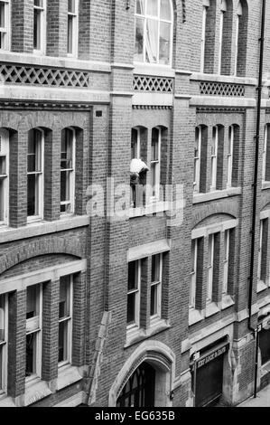 Window cleaner on very narrow ledge 3storeys up with no safety gear and man below oblivious to what is above him Stock Photo