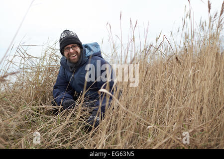 A portrait of a man laughing as he squats in long grasses Stock Photo