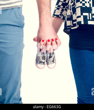 Future parents holding hands and a pair of little shoes over white background Stock Photo