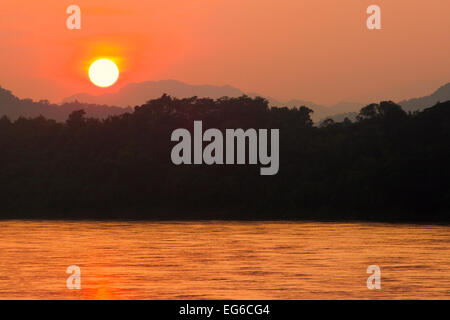 The sun begins to hide behind the dense, Laos jungle. Stock Photo