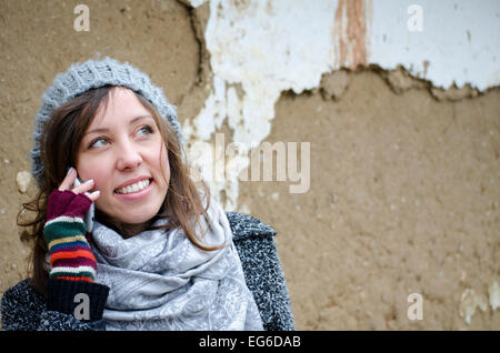 Young girl talking on the phone in front of a ruined old clay wall Stock Photo