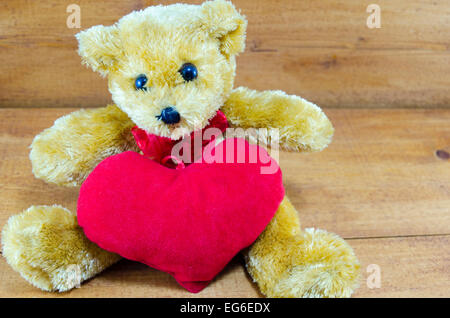 Brown teddy bear hugging a big red heart on a wooden table Stock Photo