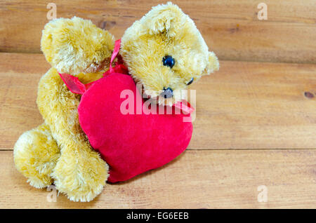 Big teddy bear lying on a red heart placed on a wooden table Stock Photo