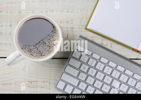 Overhead shot of a fresh brewed cup of coffee, an open book and a computer keyboard on a rustic white wood desk. Horizontal form Stock Photo