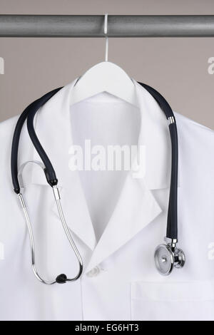 Closeup of a doctor's lab coat and stethoscope on hanger against a neutral background. White coat on a white hanger with a gray Stock Photo