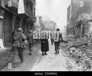 As infantrymen march through a German town, a shocked old woman stares at a the ruins. March-April 1945. Germany, World War 2. Stock Photo