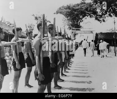 Barefoot villagers perform training drills using 'bamboo rifles' at a French Legionnaire outpost. Batri, French Indochina, Stock Photo