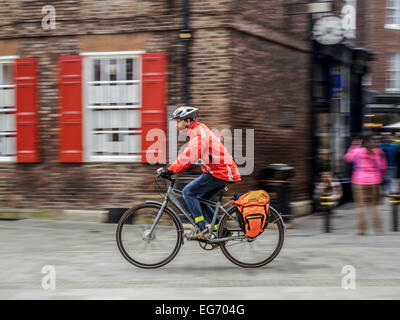 Man in orange jacket a commuter commuting riding grey gray bike cycle bicycle with motion blur of background. Stock Photo