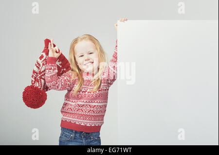 Smiling beautiful blond girl in a red winter cap and sweater with white space for text or advertisement Stock Photo