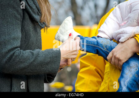 Mommy putting a shoe on baby's foot outdoors Stock Photo