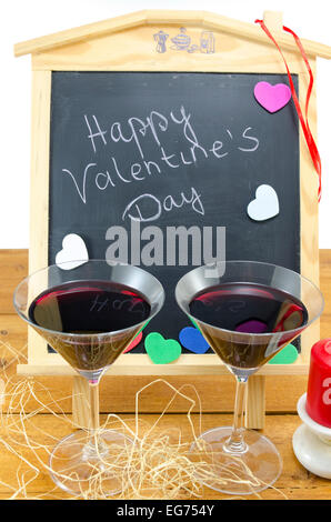 Blackboard with the words Happy Valentines written on it, decorated with hearts and and two glasses Stock Photo