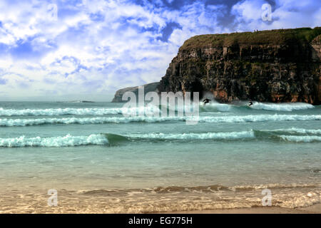 beautiful clean atlantic ocean with surfers catching the waves with cliffs in background on Irelands coast Stock Photo