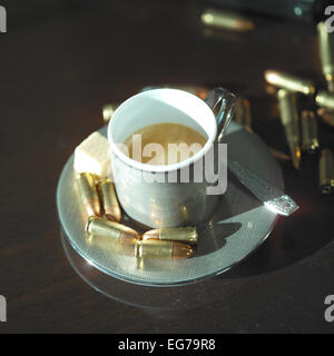 Cup of coffee and bullets on a table, overhead still life with selective focus, violence concept Stock Photo