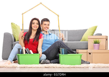 Young couple sitting by a bunch of moving boxes and making a roof over their heads with a tape measure Stock Photo