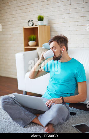 Handsome guy drinking tea or coffee while using modern gadgets at home Stock Photo