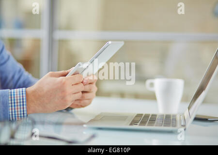 Male hands holding cellphone and touchpad with laptop near by Stock Photo