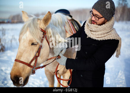 Young man in winterwear looking at horse outdoors Stock Photo