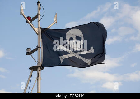 Jolly Roger flag flying on a boat in an English harbour - clearly not a classic pirate ship but perhaps someone who thinks they rule the waves Stock Photo