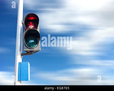 Red color on the traffic light for pedestrian, motion blurred sky. Stock Photo