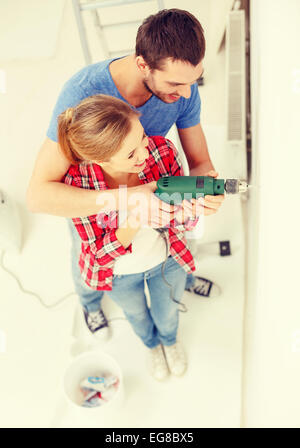 smiling couple drilling hole in wall at home Stock Photo