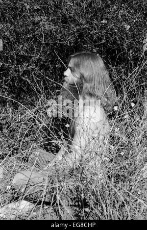 Portrait of 1960s 1970s hairy hippie man hippy male with a beard and long hair in a state of spiritual mediation sitting outdoors in brush in Berkeley, California USA 1971 KATHY DEWITT Stock Photo
