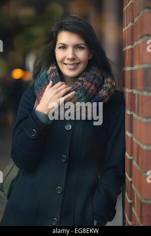 Stylish Pretty Young Woman in Autumn Fashion Leaning on red brick pillar, Looking at the Camera. Stock Photo