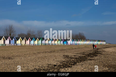 couple with dog walking along beach with Colourful Beach huts on Mersea Island,Essex,England Stock Photo