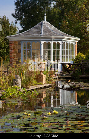 Large garden pond in summer with brick summerhouse and seating overlooking water and lillypads,Garden,Oxfordshire,England Stock Photo