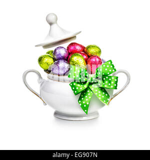 Sugar bowl with ribbon bow full of chocolate candy eggs wrapped in foil on white background. Easter themes Stock Photo