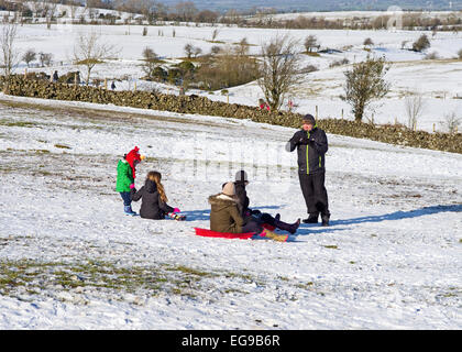 Sledging - man preparing to take photo of family with sledges on snowy hillside, Caldbeck fells, Lake District, Cumbria, England Stock Photo