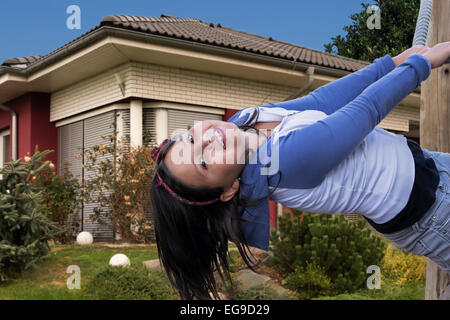 Happy young girl playing on playground in the garden in front of her home. Stock Photo