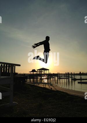 Man jumping high into sunset on beach Stock Photo